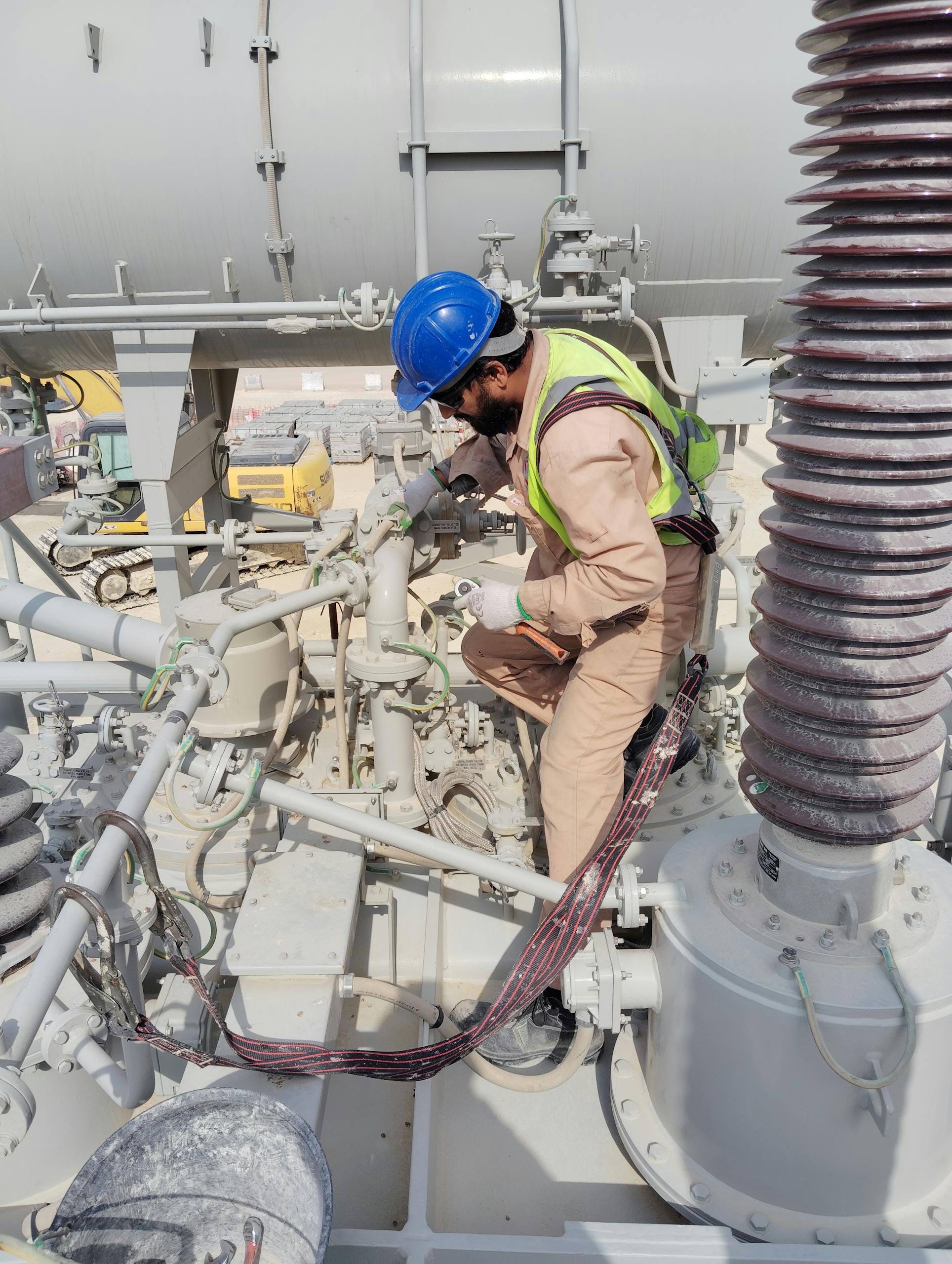 Engineer in safety gear inspecting equipment on a busy industrial construction site.
